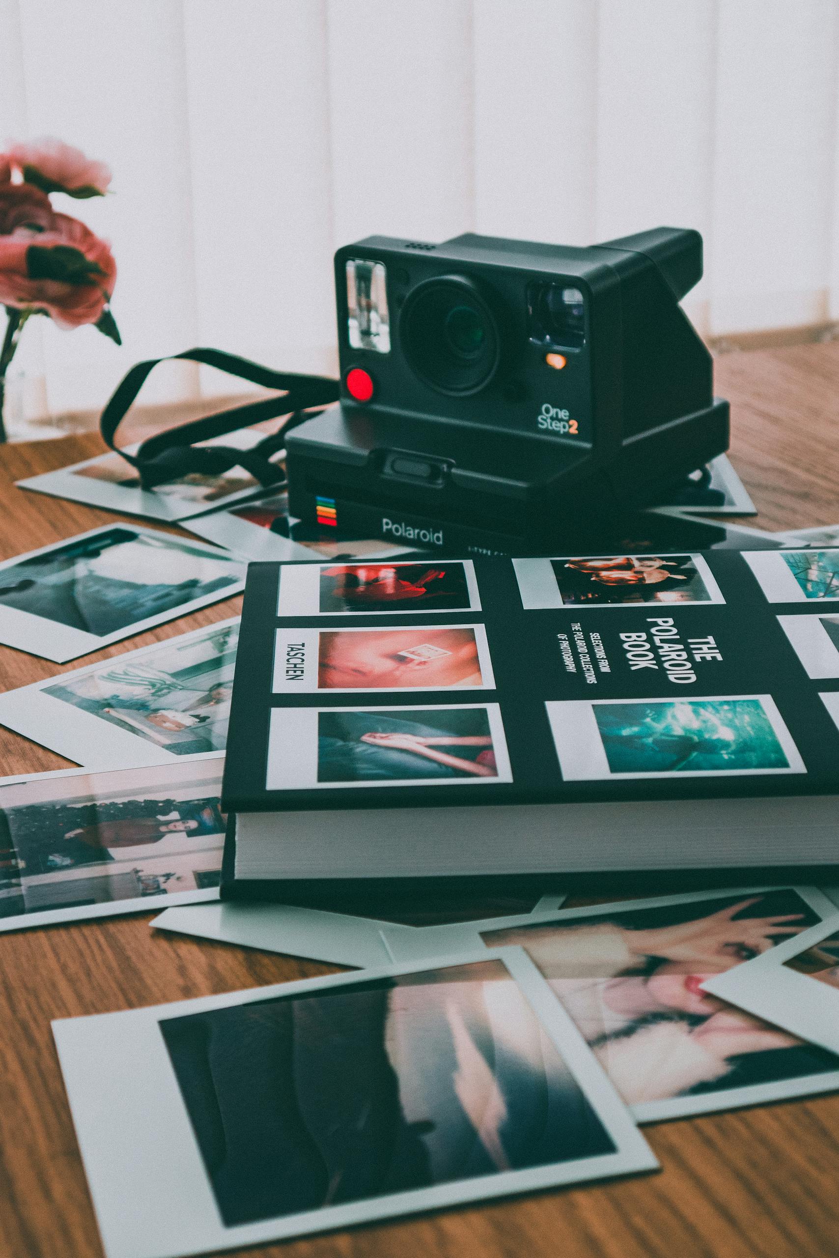A vintage Polaroid camera with scattered instant prints and a photo album on a wooden table.
